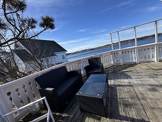 Holzterrasse mit gemütlichen Rattanmöbeln, umgeben von malerischer Küstenlandschaft bei Hitra, Norwegen. Perfekt für Angelurlaub, mit Blick auf blaues Meer und entfernte Inseln. Entspanne und genieße die Naturidylle am Wasser.