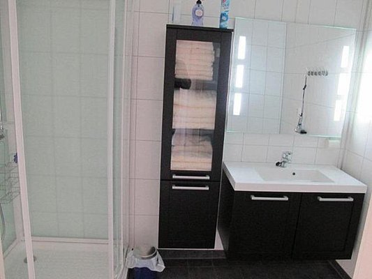 Modernes Badezimmer im Nordland-Stil, Norwegen: Duschkabine, Spiegel mit integrierter Beleuchtung, Waschbecken, dunkles Möbelstück mit Handtüchern. Elegantes, funktionales Design, ideal für Angelabenteuer und Erholung.