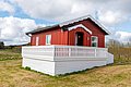 Rotes Holzhaus mit weißem Geländer in Hitra, Norwegen, eingebettet in grüne Landschaft und unter blauem Himmel. Perfekte Unterkunft für Angelreisen und Naturliebhaber. Ideal für erholsame Tage in skandinavischer Idylle.