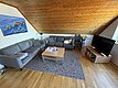 Gemütliches Wohnzimmer mit grauem Sofa, Holzmöbeln und Wandbild von Fischen. Helle, hölzerne Dachschräge und Teppich schaffen ein einladendes Ambiente in norwegischer Ferienunterkunft. Ideal für entspannte Angelreisen nach Hitra.