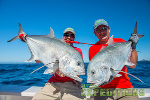 Zwei Angler halten erfolgreiche Fänge großer Fischarten vor der Küste von Mitsio Island, Madagaskar, bei strahlend blauem Himmel. Perfektes Ziel für sportliches Meeresangeln und Abenteuerlustige. Ideal für unvergessliche Angelreisen.