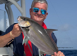 Ein Angler hält stolz einen gefangenen Fisch auf einem Boot. Der blaue Ozean und der Himmel von Sao Vicente, Kapverden, sind im Hintergrund zu sehen. Perfekter Spot für ein aufregendes Angelabenteuer.
