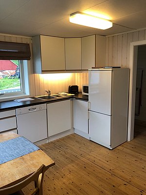 Helle, gemütliche Küche in Nord-Norwegen mit Holzfußboden, weißer Ausstattung und modernen Geräten. Fenster mit Blick ins Grüne, warmes Licht sorgt für einladende Atmosphäre. Perfekt für einen entspannten Angelurlaub in atemberaubender Umgebung.