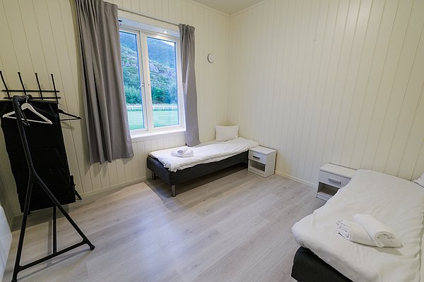 Gemütliches, helles Zimmer in Nordland, Norwegen. Zwei Einzelbetten, Fensterblick ins Grüne, minimalistisches Design. Perfekte Unterkunft für Angelreisen und Erholung in skandinavischer Naturkulisse. Nachhaltig und erholsam wohnen mitten im Abenteuer.
