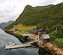 Holzhaus und Steg mit Boot vor grüner Bergkulisse am ruhigen Fjord in Nord-Norwegen. Perfekt für Angelurlaub und Erholung in unberührter Natur. Majestätische Landschaften bieten Abenteuer und Ruhe zugleich. Ideal für Meeresangelnliebhaber.