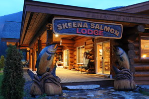 Das Bild zeigt die Skeena Salmon Lodge in Kanada, umgeben von malerischer Natur. Rustikale Holzkonstruktion mit eindrucksvollen Fischskulpturen, ideal für Angelurlaube am Skeena River. Perfekt für Abenteuerliebhaber und Angler.