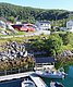 Küstenlandschaft in Nord-Norwegen mit malerischem Hafen, Booten und roten Hütten. Umgeben von grünen Hügeln, lädt die Szenerie zu Angelabenteuern ein. Perfekter Ausgangspunkt für Angelreisen in fischreiche Gewässer der norwegischen Fjorde.