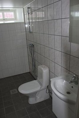 Helles Badezimmer in Nord-Norwegen mit moderner Ausstattung: weiße Fliesen, Toilette, Waschbecken und Dusche. Praktische und saubere Sanitäreinrichtungen für komfortable Aufenthalte während der Angelreise.