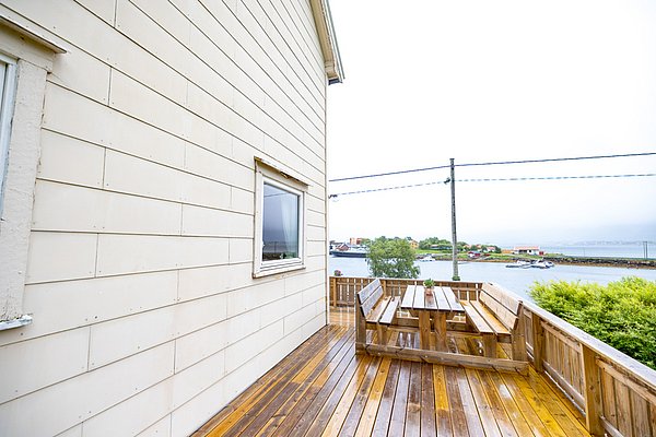 Holzterrasse eines Hauses in Nordland, Norwegen, mit Blick auf das Wasser und bunte Häuser im Hintergrund. Ruhige Atmosphäre ideal für Angelurlaube. Perfekte Kombination aus Natur und Entspannung für Deine nächste Reise.