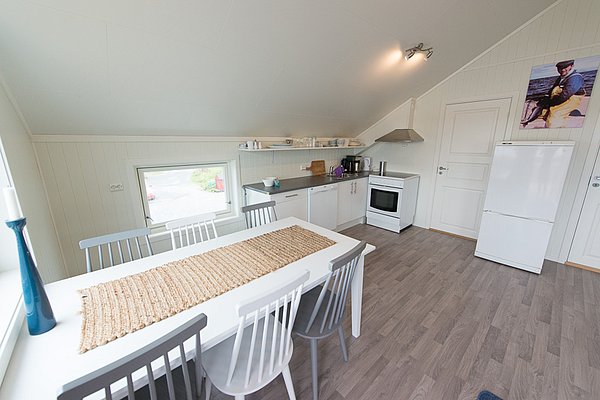 Helle, moderne Küchenzeile in Nordland, Norwegen. Ausgestattet mit Esstisch, Stühlen, und Einbaugeräten in gemütlichem skandinavischem Stil für Angelreisen. Fensterblick bietet natürliche Beleuchtung und Landschaftsansicht. Ideal für entspannten Angelurlaub.