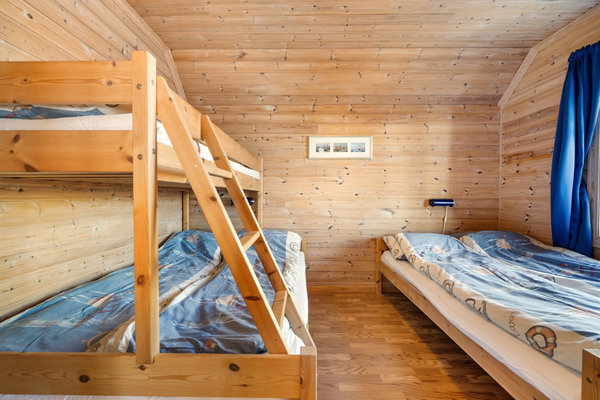 Gemütliches Schlafzimmer in einer Hütte aus Südwest-Norwegen mit Holzwänden, Etagenbett und Einzelbett. Ideal für Angelurlauber, die Komfort und rustikale Atmosphäre suchen. Perfekt für erholsame Nächte nach erfolgreichen Angelausflügen.