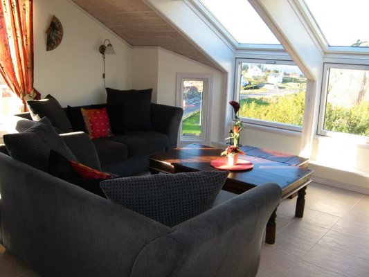 Gemütliches Wohnzimmer in Südwest-Norwegen mit Panoramafenstern, bequemen Sofas und Blick auf malerische Landschaft. Ideal für Entspannung nach Angeltouren. Perfekte Kombination aus Komfort und Naturerlebnis in norwegischem Ambiente.