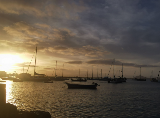 Sonnenuntergang in São Vicente, Kapverden: Boote schaukeln sanft im Hafen, während goldene Sonnenstrahlen den Himmel dramatisch erleuchten. Perfekte Kulisse für einen ruhigen Angelurlaub mit Meeresangeln und Entspannung.