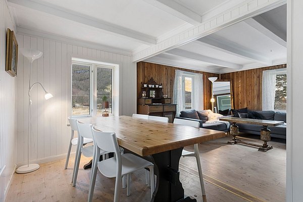 Gemütliches skandinavisches Interieur in Nordland, Norwegen. Helles Wohnzimmer mit Holzwänden, großem Esstisch und bequemen Sofas. Fenster bieten Blick auf idyllische Landschaft. Perfekt für entspannten Angelurlaub und Erholung in der Natur.