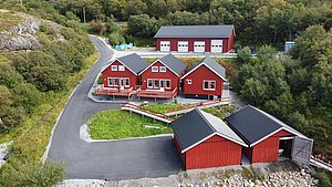 Luftaufnahme von roten, traditionellen Hütten in Hitra, Norwegen, umgeben von grüner Natur und felsiger Landschaft. Perfekter Ausgangspunkt für Angelabenteuer in der Region. Ideal für Erholung in idyllischer skandinavischer Umgebung.