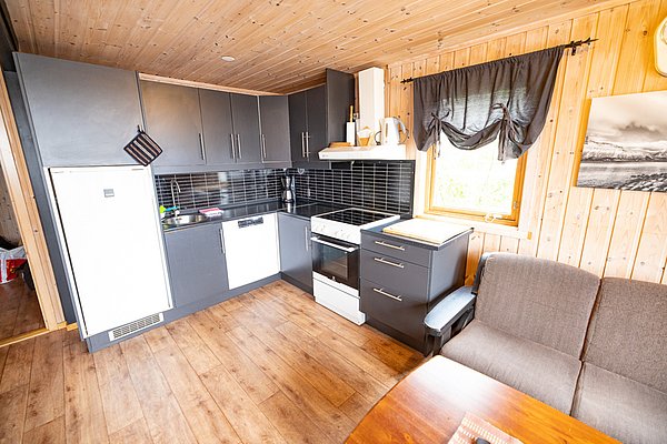 Gemütliche Holzhütte in Nordland, Norwegen, mit moderner Küche, Sofa und Panoramablick. Ideal für Angelurlaube, umgeben von Natur und Ruhe. Perfekter Ausgangspunkt für Abenteuer und Entspannung.
