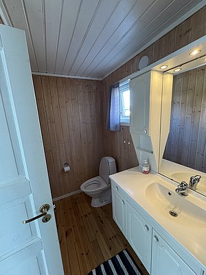 Helles, modernes Badezimmer in Hitra, Norwegen, mit Holzverkleidung, weißem Waschtisch, Spiegel und WC. Ideal für einen komfortablen Angelurlaub.
