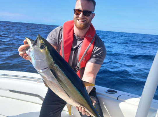 Ein begeisterter Angler hält stolz einen großen Thunfisch auf einem Boot vor der Küste von São Vicente, Kapverden. Perfekter Angelurlaub im blauen Ozean mit sonnigem Himmel.