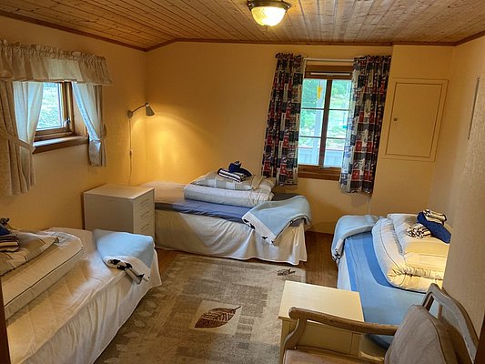 Gemütliches Schlafzimmer in Hitra, Norwegen mit Holzdach, vier Einzelbetten, Teppich und Fenstern. Ideal für Angelurlaub und Gruppenreisen. Perfekte Unterkunft für Entspannung nach einem erfolgreichen Angeltag.