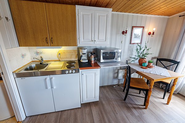 Gemütliche Küchenzeile in einer Ferienunterkunft in Hitra, Norwegen. Ausgestattet mit Herd, Spüle, Mikrowelle, Kaffeemaschine und Esstisch. Perfekt für Angler, die Entspannung und Abenteuer suchen. Ideal für einen erholsamen Angelurlaub.