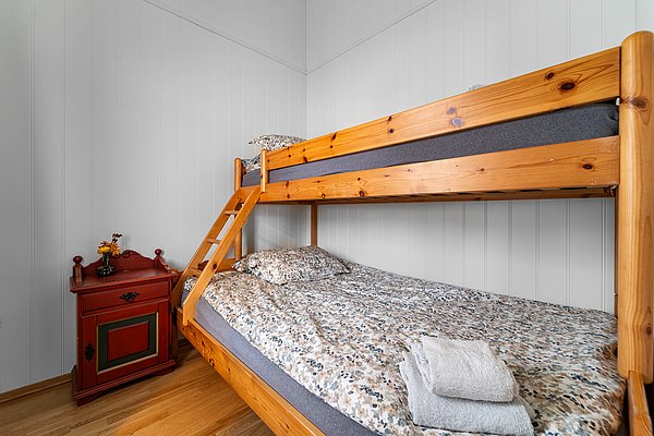 Kompaktes Schlafzimmer mit Etagenbett aus Holz und gemütlicher Bettwäsche in Nord-Norwegen. Rote Kommode mit Vase und Blumen verleiht rustikalen Charme. Perfekt für erholsame Nächte während Angelreisen.