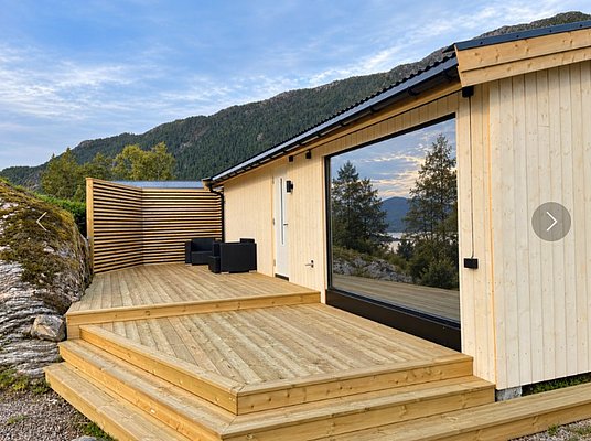 Modernes Ferienhaus aus Holz in Hitra, Norwegen, mit Terrasse und Panoramablick auf Berge und See. Ideal für Angelreisen und Naturliebhaber, die Komfort und atemberaubende Landschaften suchen. Perfekter Ausgangspunkt für Abenteuer.