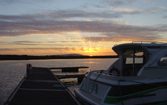 Ein Boot liegt an einem Steg bei Sonnenuntergang auf einem ruhigen Gewässer, während der Himmel in warmen Farben leuchtet.