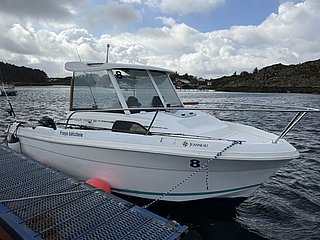 Weißes Angelboot am Steg in Süd-Norwegen, umgeben von bewölktem Himmel und felsiger Küste. Perfekt für entspannte Angelreisen und Erkundungen der norwegischen Landschaft.