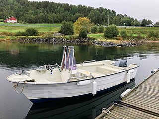 Ein weißes Angelboot liegt ruhig an einem Holzsteg in Südwest-Norwegen. Im Hintergrund sind grüne Bäume und ein rotes Haus zu sehen, perfekte Kulisse für entspannte Angelabenteuer.