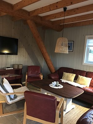 Gemütliches Wohnzimmer in einem skandinavischen Holzhaus auf Hitra, Norwegen. Rustikale Einrichtung mit bequemen Ledersofas, Holzbalken und sanfter Beleuchtung. Ideal für entspannte Angelreisen und Erholung in der Natur.