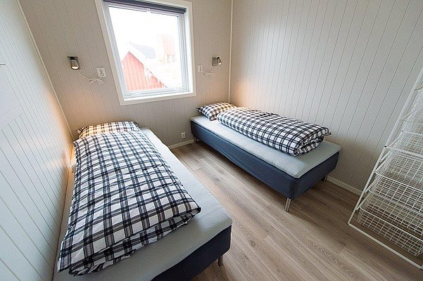 Gemütliches Schlafzimmer in Nordland, Norwegen mit zwei Einzelbetten, karierten Bettdecken und Holzvertäfelung. Helles Fenster bietet Blick nach draußen, ideale Unterkunft für Angelurlaub in idyllischer Umgebung.