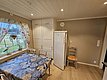 Gemütliche Küche in Südwest-Norwegen mit Tisch, buntem Tischtuch und Fensterblick ins Grüne. Helle Einrichtung, Kühlschrank und dekorative Vorhänge schaffen entspannte Atmosphäre. Ideal für Angelurlaub und Erholung.