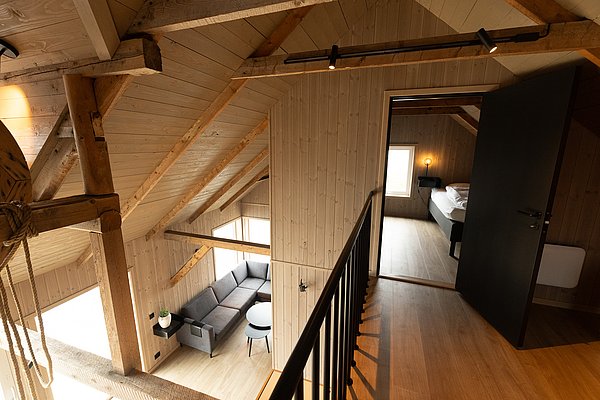 Gemütliches nordisches Holzinterieur in Nordland, Norwegen. Offener Wohnbereich mit Sitzgruppe und modernem Schlafzimmer auf einer Empore. Ideal für erholsame Angelurlaube und Naturerlebnisse.