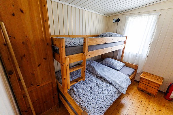 Gemütliches Schlafzimmer in Hitra, Norwegen, mit Etagenbett aus Holz, Schrank und Nachttisch. Ideal für Angelreisen, bietet komfortable Unterkunft in rustikalem Ambiente. Perfekt zum Entspannen nach einem erfolgreichen Tag am Meer.