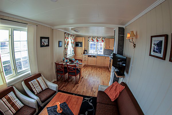 Gemütliches Wohnzimmer in Nord-Norwegen mit moderner Küche, Esstisch und gemütlicher Sitzecke. Helle Holzmöbel, dekorative Vorhänge und große Fenster schaffen eine einladende Atmosphäre. Ideal für erholsame Angelurlaube.