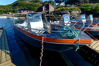 Angelboot im Hafen von Südwest-Norwegen. Ideal für Meeresangeln, umgeben von grünen Hügeln und roten Häusern. Perfekter Ausgangspunkt für Abenteuer auf dem Wasser. Maritime Idylle und Fischreichtum erwarten Dich hier.