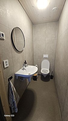 Modernes Badezimmer in der Region Hitra, Norwegen. Mit schlichtem Design, Waschbecken, rundem Spiegel und WC. Helle Decke, graue Fliesen, ideal für komfortablen Angelurlaub. Perfekt für Entspannung nach einem erfolgreichen Angeltag.
