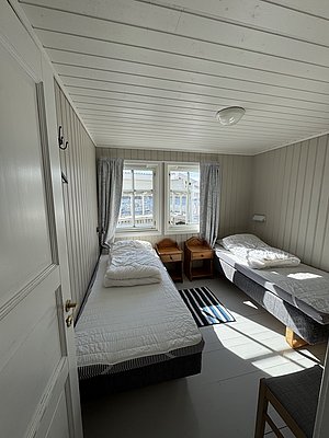 Gemütliches Schlafzimmer in einer norwegischen Hütte auf Hitra, mit zwei Einzelbetten, weißen Holzverkleidungen und Fenstern mit Ausblick ins Freie. Ideal für entspannten Angelurlaub.