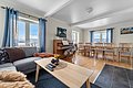 Gemütliches Wohnzimmer in Nord-Norwegen mit hellen Holzmöbeln, Klavier, großem Esstisch und Panoramablick auf verschneite Berge durch große Fenster. Perfekt für einen erholsamen Angelurlaub in skandinavischer Atmosphäre.