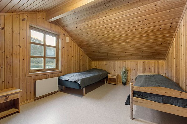 Gemütliches Schlafzimmer in Nordland, Norwegen, mit zwei Einzelbetten und Holzverkleidung. Ideal für Angelreisende, die Komfort und Ruhe suchen. Große Fenster bieten natürliche Lichtdurchflutung und maximale Entspannung. Perfekte Unterkunft für unvergessliche Angelabenteuer.