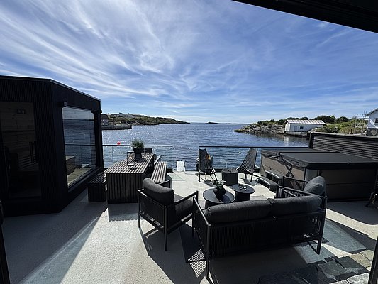 Moderne Terrasse mit stilvollen Möbeln bietet atemberaubenden Blick auf norwegische Fjordlandschaft, umgeben von klarem Himmel und ruhigem Wasser. Perfekt für Angelurlaub oder Entspannung in Südwest-Norwegen.