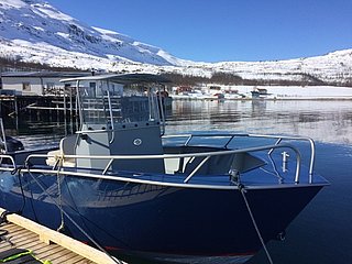 Blaues Angelboot im Hafen von Nord-Norwegen, umgeben von schneebedeckten Bergen und klarem Wasser. Perfekter Ausgangspunkt für Meeresangeln und Abenteuer in atemberaubender Winterlandschaft.