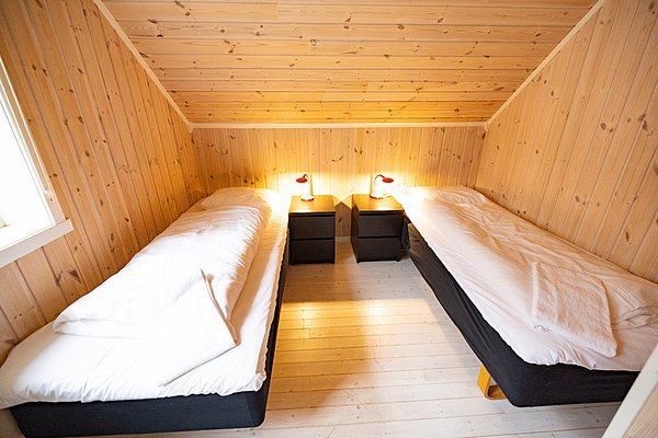 Gemütliches Schlafzimmer in Nordland, Norwegen mit zwei Einzelbetten aus Holz, warm beleuchtet. Ideal für Angelurlauber, die Entspannung nach einem erfolgreichen Angeltag suchen. Perfekte Mischung aus Komfort und nordischer Gemütlichkeit.