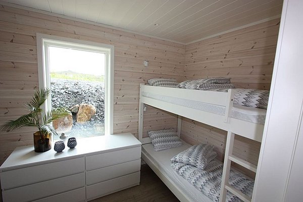 Gemütliches Schlafzimmer mit Holzvertäfelung in Nordland, Norwegen. Stockbetten, eine Kommode und ein Fenster mit Natursteinblick schaffen eine einladende Atmosphäre für Erholung inmitten der nordischen Wildnis. Ideal für Gäste auf Angelreisen.
