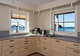 Moderne Küche mit Holzschränken und Meerblick in Hitra, Norwegen. Helle Fenster lassen das Tageslicht herein, ideal für entspannte Momente nach einem erfolgreichen Angelausflug. Perfekte Kombination aus Komfort und Naturerlebnis.