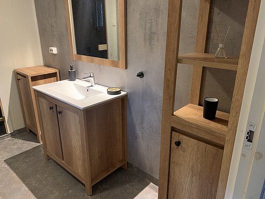 Modernes Badezimmer in Nord-Norwegen mit Holzschränken, Waschbecken und Spiegel. Dezente Beleuchtung kombiniert mit natürlichen Materialien sorgt für gemütliche Atmosphäre. Ideal für entspannte Stunden nach einem Angeltag in der malerischen Umgebung.