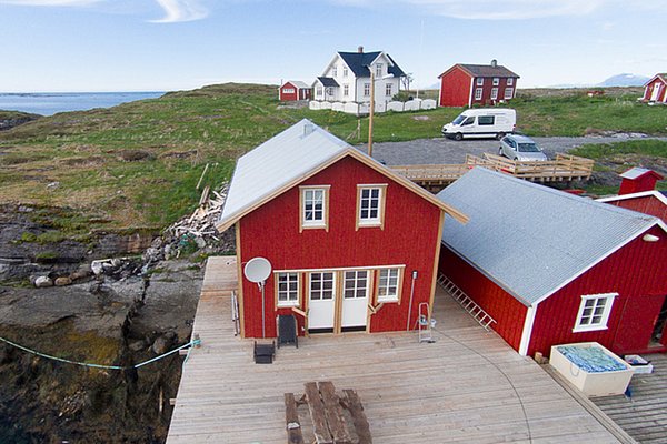 Rote Holzhäuser direkt am Meer in Nordland, Norwegen. Malerische Landschaft mit grünen Hügeln und felsigen Küsten. Ideal für einen erholsamen Angelurlaub und unvergessliche Outdoor-Abenteuer. Perfekt für Natur- und Meeresliebhaber.
