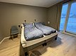 Gemütliches Schlafzimmer in Hitra, Norwegen: Doppelbett mit blauen Bettdecken, zwei Stühlen, helle Holzböden und großes Fenster mit Winterblick. Ideal für entspannten Angelurlaub und Erholung in skandinavischer Natur.
