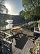 Holzterrasse in Hitra, Norwegen: Ein idyllischer Blick auf ein ruhiges Gewässer, umgeben von einem sonnigen Pier, Bäumen und einem charmanten roten Bootshaus – perfekt für entspannte Angel- und Naturerlebnisse.