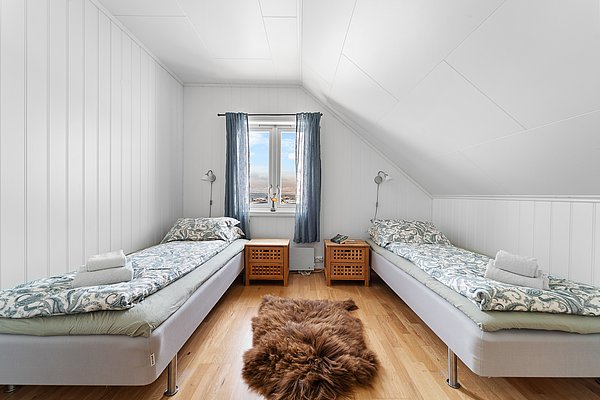 Gemütliches Schlafzimmer in nordnorwegischer Ferienhütte mit zwei Einzelbetten, hellem Holzboden und Panoramablick aufs Meer. Ideal für Angler, die entspannte Nachtruhe suchen. Ein Teppich sorgt für Wärme und Komfort.